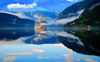 Nordeuropa-Kreuzfahrt im Fjord Großes Kreuzfahrtschiff in einem ruhigen Fjord, umgeben von steilen, grünen Bergen, das sich im Wasser spiegelt.