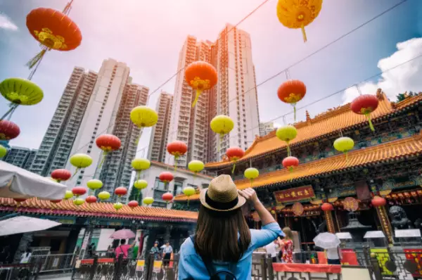 Eine junge Frau steht in Hongkong und blickt auf einen Wolkenkratzer. Über ihr hängen Lampions an einer Leine.