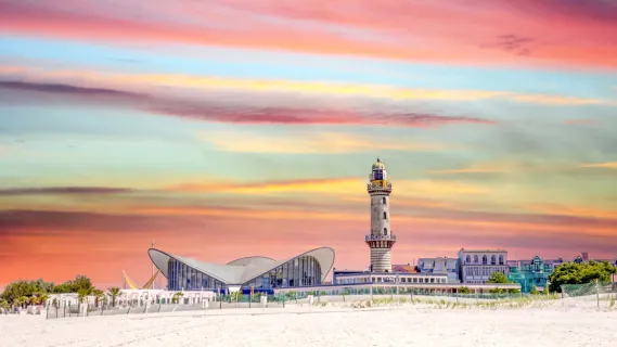 Kreuzfahrt Warnemünde – Die Wahrzeichen Leuchtturm und Teepott am Strand Der historische Warnemünder Leuchtturm und der markante Teepott am breiten, feinsandigen Ostseestrand unter einem farbenfrohen Abendhimmel – ideal für einen Landausflug auf eigene Faust.