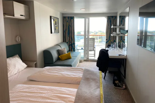 Doppel kabine auf Mein Schiff 7. Fotografiert von einer Ahoi-Schiff Mitarbeiterin. Blick in eine Doppelkabine auf <i>Mein Schiff 7</i> mit einem Bett, Sofa, Panoramafenster und Balkon.