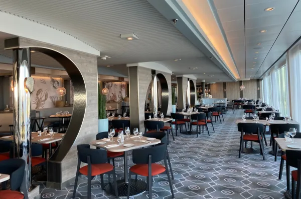 Restaurant auf Mein Schiff 7. Fotografiert von einer Ahoi-Schiff Mitarbeiterin. Ein Restarant mit mordernen Möbeln auf der <i> Mein Shhiff 7 </i>. kleine Tische mit je vier Stühlen sind an einer Fensterfront aufgereiht.