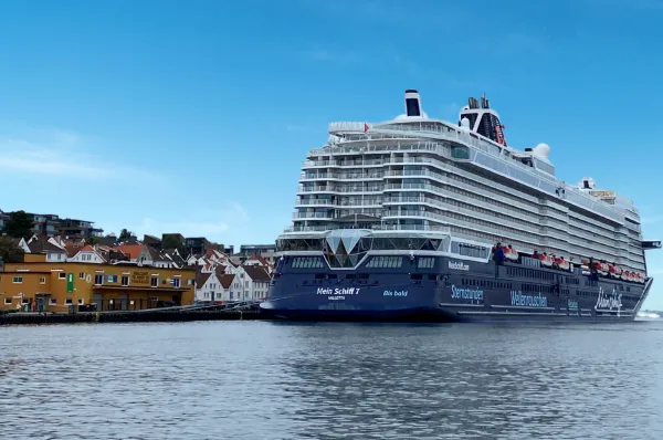 Heck der Mein Schiff 7. Fotografiert von einer Ahoi-Schiff Mitarbeiterin. Die Heckansicht von <i>Mein Schiff 7</i>. Unten am Rumpf steht in weiß auf blau "Mein Schiff 7 Valletta" und in türkis auf blau Bis bald. Das Schiff liegt am Hafen einer Stadt mit kleinen Häusern.