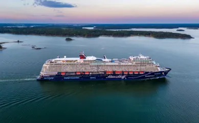 Seitenansicht der <i>Mein Schiff 7</i> vor der Küste Finnlands, während im Hintergrund langsam die Sonne versinkt.