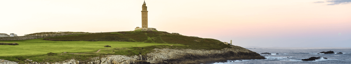 Linksseitig sehen Sie grüne Lanschaft. Mittig im Bild sieht man in der Ferne den Herkules Turm welcher im Sonnenuntergang erstrahlt. Rechts ist ein Meerabschnitt