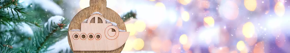 Hölzerner Christbaumschmuck in Form einer Kugel mit einem Holzschiff darauf hängt an einem Tannenzweig vor einem lila Hintergrund mit goldgelbem Glitzer.