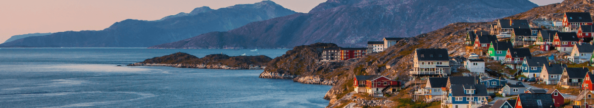 Links im Bild ist das Meer zu sehen. Recht im Vordergrund die Stadt Nuuk durch eine Vielzahl von Häusern und Dächern und recht im Bildhintergrund sieht man Gebirge