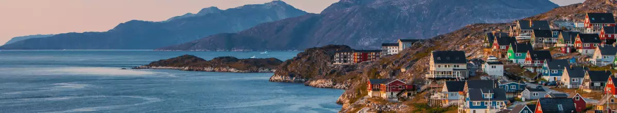 Links im Bild ist das Meer zu sehen. Recht im Vordergrund die Stadt Nuuk durch eine Vielzahl von Häusern und Dächern und recht im Bildhintergrund sieht man Gebirge
