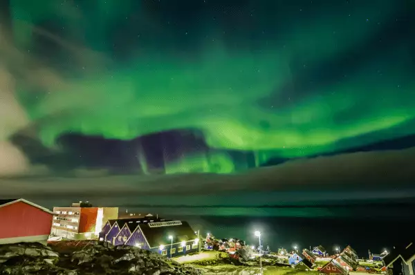 Polarlichter Auf dem Bild erstrahlen die grünen Polarlichter in voller Fülle. Sie bringen den Himmel zum leuchten. Des weiteren sieht man rote Häuser, wekche zwischen Grünflächen stehen