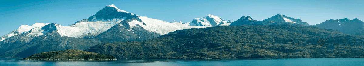 Links sieht man die gefrohrene Gbirgskette. Davor gelagert einige Berge, welche keinen Schnee auf sich tragen. Im Vordergrund ist das Meer zu sehen.