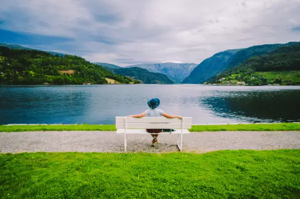 Eine Frau sitzt auf einer weißen Bank vor einem See in Ulvik auf welchen Sie herausschaut.
