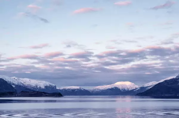 Hinter dem Hardangerfjord sieht man die großen weißen Gebirge hervorklingeln. Im Rücken der Gebirgskette geht die Sonne unter.