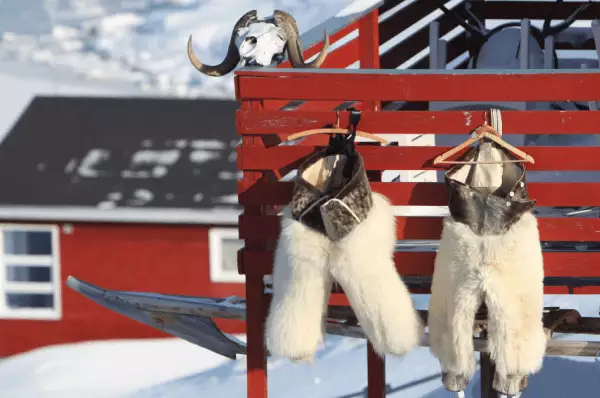 Inuit An der Veranda eines kleinen roten Häuschens hängt Fellkleidung der Inuit. Um das Häuschen herum liegt eine große Masse an Schnee.
