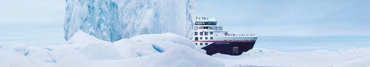 Der Bug der HANSEATIC inspiration schaut hinter einem Eisberg hervor und fährt weiter durch das Eismeer.