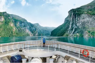 Auf dem Deck der HANSEATIC inspiration steht eine Frau erwartungsvoll am Bug, mit Blick auf die schroffen Felsen Norwegens.