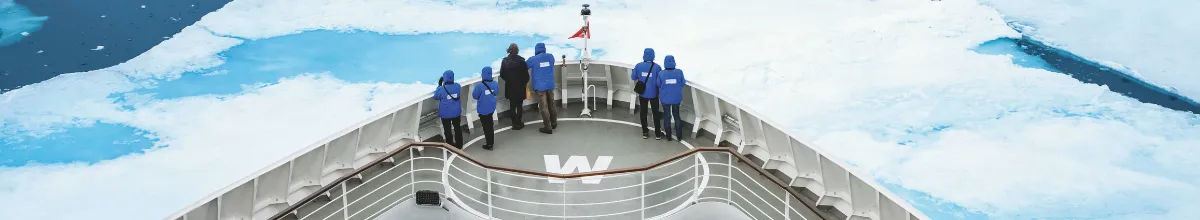 Gäste in blauen Parkas stehen am Bug der HANSEATIC nature und blicken über Packeis und türkisfarbenes Wasser.
