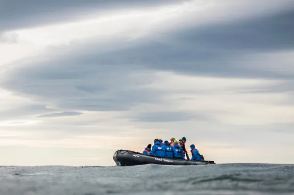 Zodiac-Fahrt auf offener See Gäste in blauen Jacken sitzen in einem Zodiac der HANSEATIC nature auf offener See unter dramatischem Wolkenhimmel.