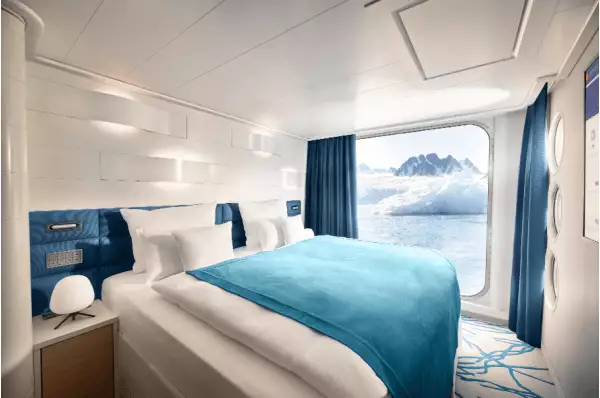 Die Juniorsuite ist mit Blick aufs Meer ausgerichtet. Ein großes Bett steht inmitten des Bildes und ist mit einer blauen Decke geschmückt.
