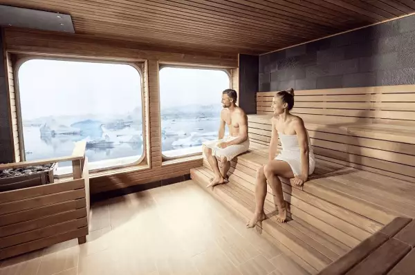 Eine Frau und ein Mann sitzen in der Sauna der HANSEATIC nature. Aus der Sauna hat man Blick in Richtung Meer.