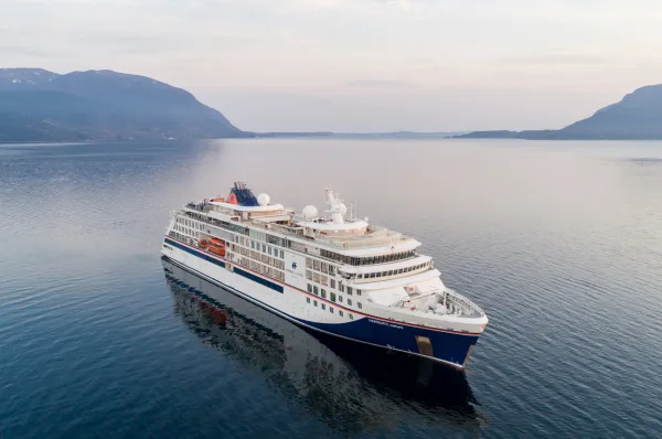 HANSEATIC nature in ruhiger Fjordlandschaft Die HANSEATIC nature von Hapag-Lloyd Cruises liegt bei diesigem Licht zwischen bewaldeten Bergen auf spiegelglattem Wasser.