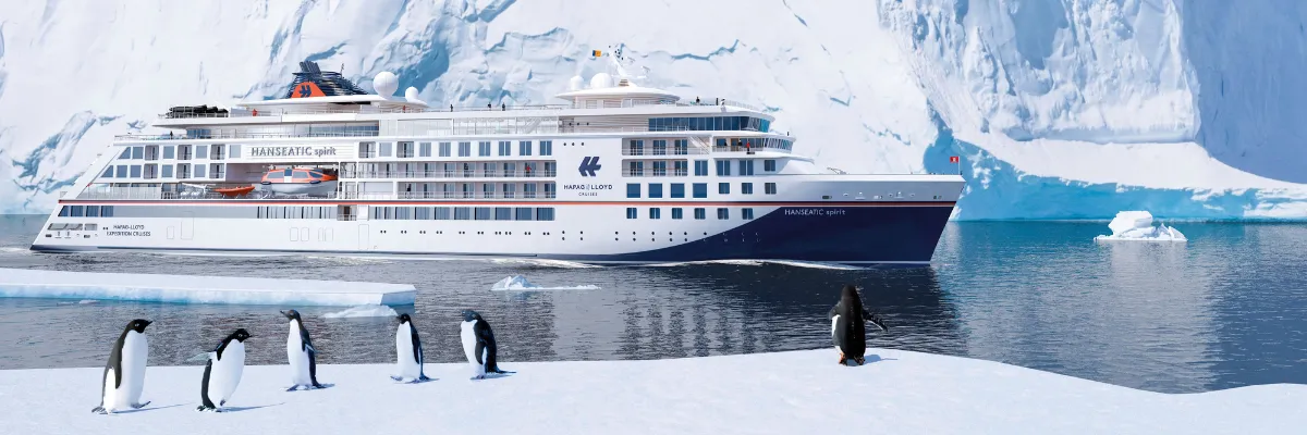 Antarktiskreuzfahrt Ein riesiger Eisberg ragt aus dem Meer hervor. Davor fährt die HANSEATIC spirit durch die Eisschollen und Pinguine laufen durch die Gegend.