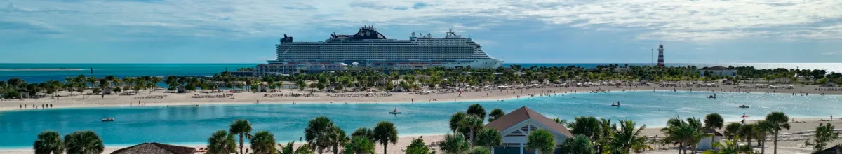 Panoramablick auf die Lagune und den weißen Sandstrand der MSC Privatinsel Ocean Cay auf den Bahamas. Im Vordergrund baden Menschen im türkisfarbenen Wasser, gesäumt von Palmen. Im Hintergrund liegt ein großes MSC Kreuzfahrtschiff am Pier.
