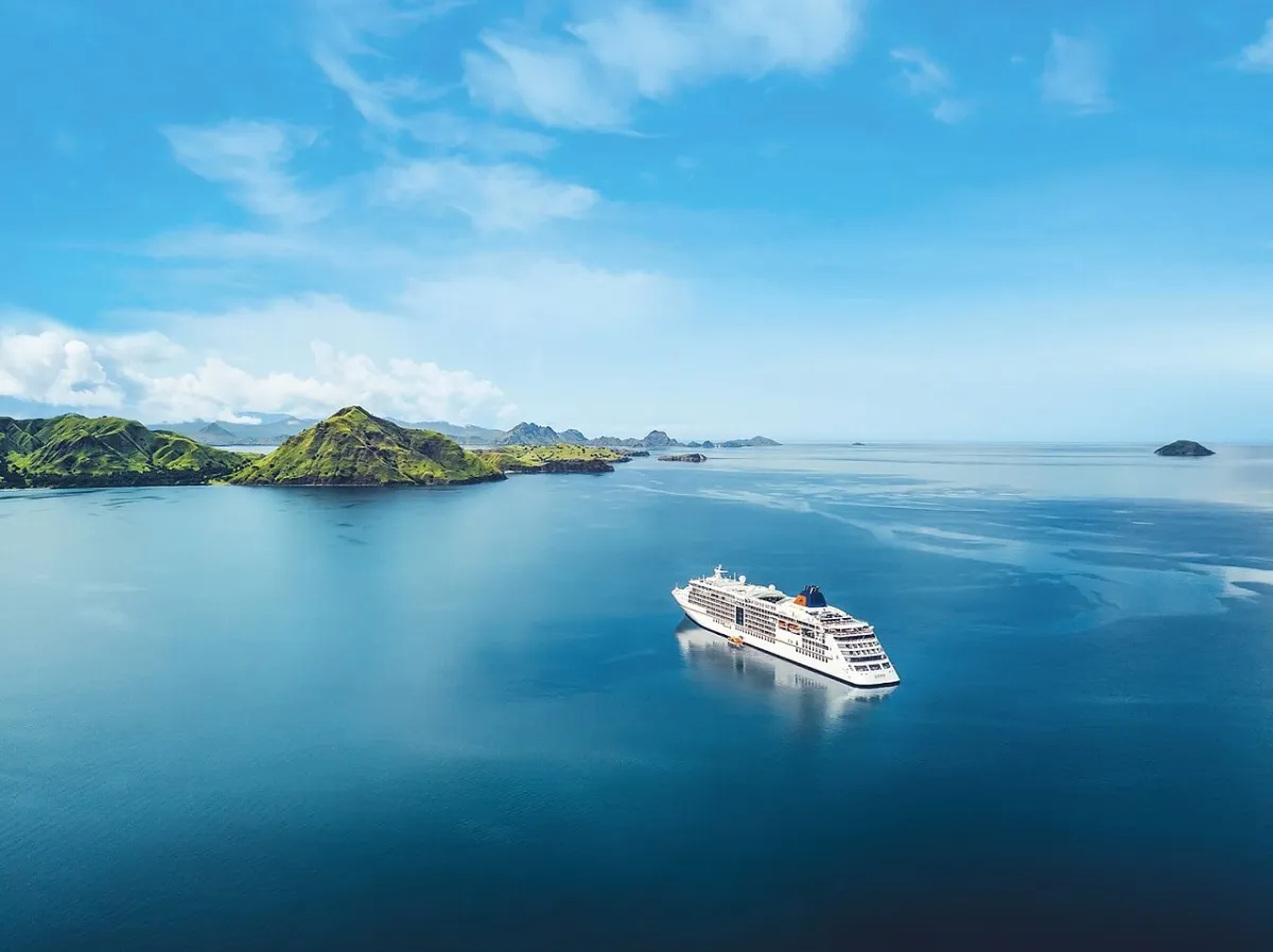 MS Europa 2 Das Schiff MS Europa 2 gleitet durch das tiefblaue Wasser. Im Hintergrund ist eine Insel zu sehen.