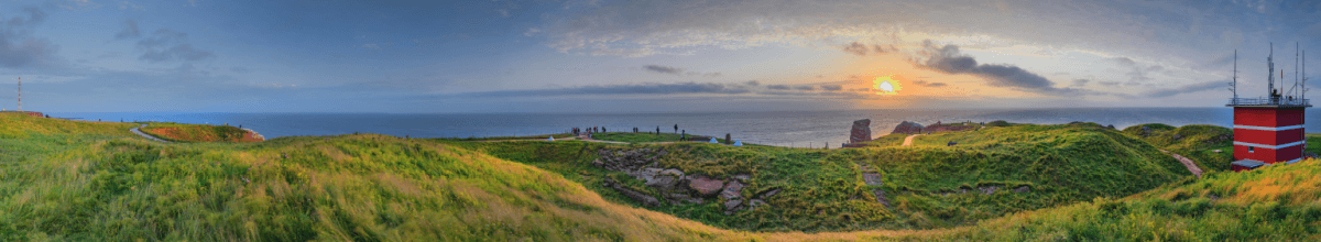 Zwischen grünen Hügeln geht die Sonne über Helgoland auf.