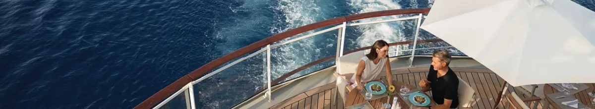 Ein Paar genießt ein entspanntes Mittagessen auf dem Sonnendeck eines Hapag-Lloyd Schiffes mit Blick auf das Meer, passend zu den neuen erweiterten Inklusivleistungen.