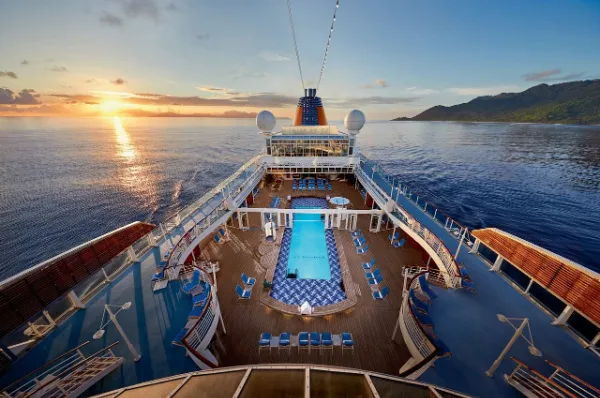 Blick über das sonnendurchflutete Pooldeck und den markanten orangen Schornstein der MS Europa auf das weite Meer bei Sonnenuntergang.