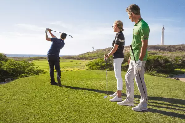 Auf einem Golfplatz steht ein Mann, der  grade abschlägt. Hinter ihm stehen weitere Golfspieler.