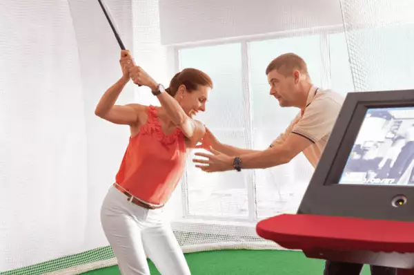 An Board des Kreuzfahrtschiffes steht eine Frau am Golfsimulator und wird von einem PGA Profi in ihrer Technik verbessert.