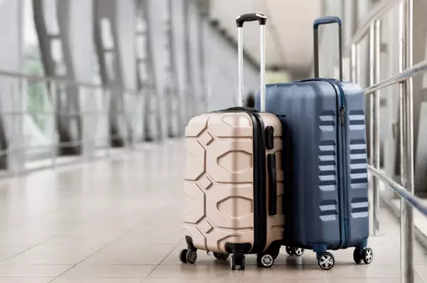 Man sieht zwei Koffer, welche auf einem Gang im Flughafen stehen. Der eine ist goldmiliert und der andere marine blau.