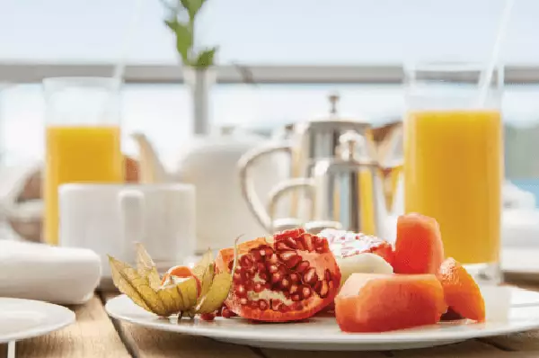 Frühstück Auf einem Holztisch an Bord stehen O-Saft, Kaffee und Tee bereit. Zusätzlich befindet sich auf dem Tisch ein Teller vom Frühstücksbuffet. Er ist voller Obst und Müsli.