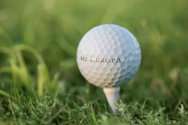 Golfball mit der Aufschrift MS Europa Auf einem Tee, welcher im Gasen steckt ist ein weißer Golfball mit der Aufschrift MS Europa.