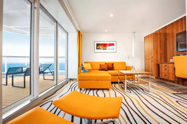 AIDA Suite in gelber Optik mit moderner Couch, Balkon mit Liegestühlen