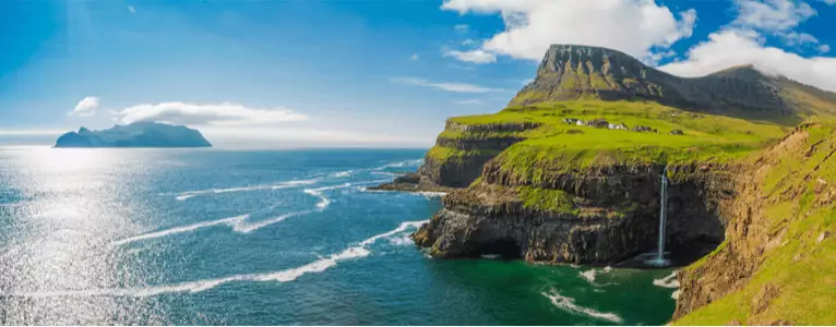 Dänemarks Küsten Die felsige Küste Dänemarks mit seichten Wellen im Meer und einer Insel etwas weiter weg.