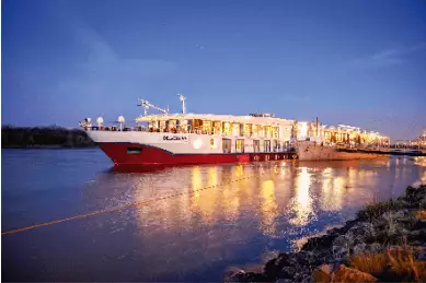 Die hell erleuchtete MS BELVEDERE auf einem Fluss in der Abenddämmerung.