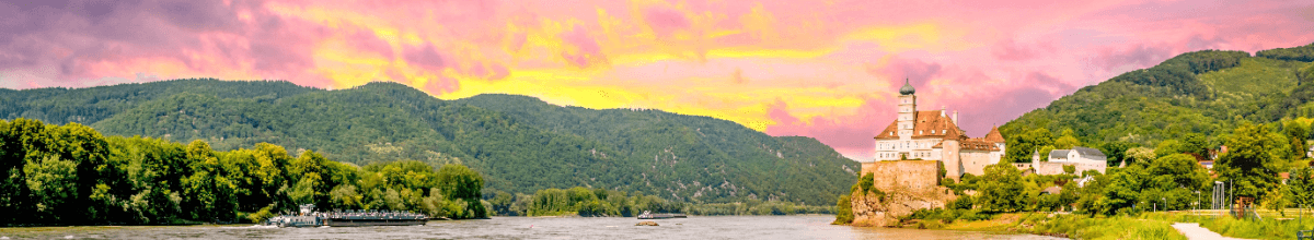 Donaulandschaft im Abendrot: Der Fluss schlängelt sich vorbei an bewaldeten Hängen und Schloss Schönbühel, das am rechten Ufer gelegen ist.