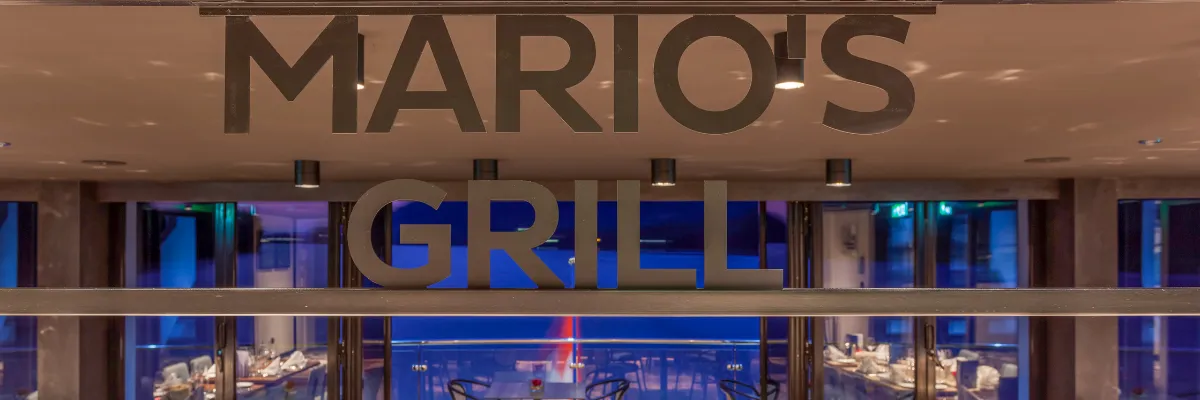 Schriftzug des Spezialitätenrestaurants Mario's Grill an Bord der nickoSPIRIT mit Blick auf den stilvoll eingedeckten Restaurantbereich
