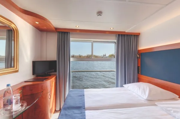 Zu sehen ist ein Doppelbett mit Aussicht auf den Fluss. Farbtechnisch ist es sehr schlicht gehalten.