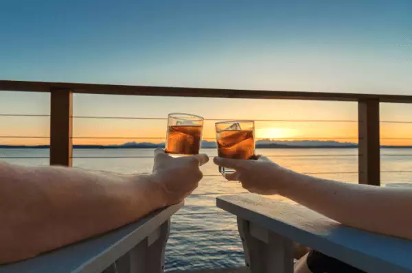 Getränke bei Sonnenuntergang Arme von zwei Personen die mit einem Getränk bei Sonnenuntergang mit Bick aufs Meer anstoßen.