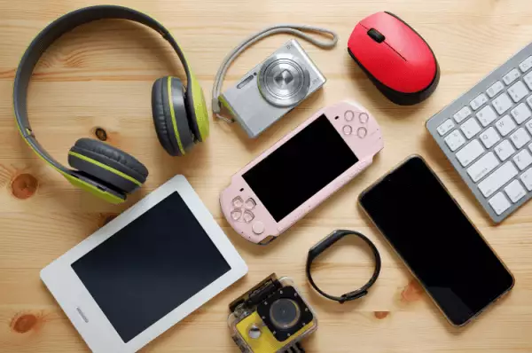 Elektronische Artikel Kopfhörer, Kamera, Tablet, PC-Maus, Smartphone, Smartwatch, Spielkonsole, PC- Tastatur liegen auf einem Tisch verteilt.