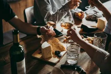 Zu sehen ist eine Themenreise zum Thema Wein. An einem Tisch sitzen Menschen, welche mit einem Glas Wein anstoßen und Käse genießen.