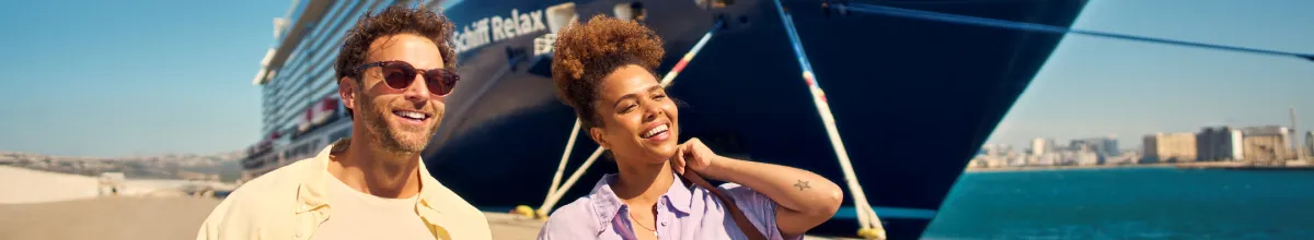 Ein glückliches Paar genießt den Sonnenschein im Hafen vor dem modernen Kreuzfahrtschiff <i>Mein Schiff Relax</i>.