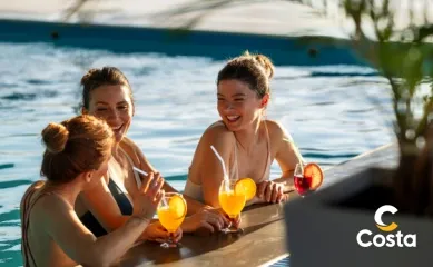 Drei Frauen in einem Pool auf einem der Costa Schiffe lehnen sich am Beckenrand an und trinken fruchtige Cocktails.