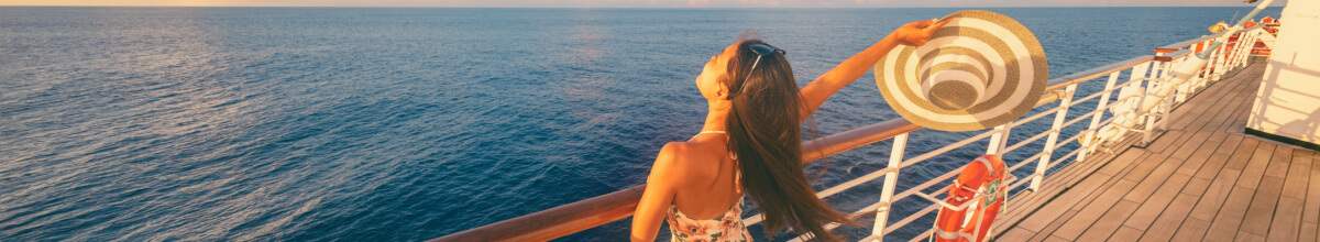 Frau auf Kreuzfahrtschiff mit Sonnenhut in der Hand und Blick auf Meer