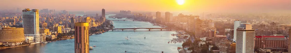 Auf der Skyline der Stadt geht die Sonne unter. Man sieht ein romantisches Farbenspiel zwischen den Hochhäusern entlang des Flusses.