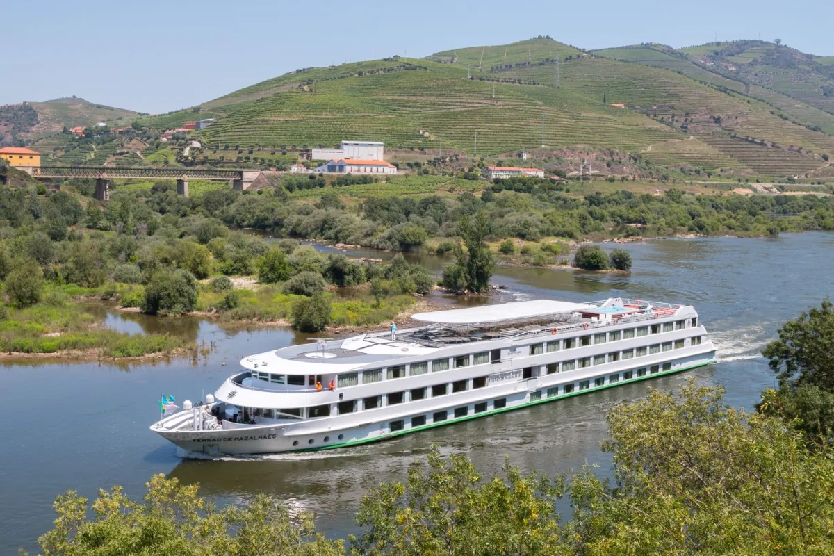 Flussschiff auf malerischem Fluss – Panoramablick auf Natur und Landschaft Flussschiff auf ruhigem Fluss mit grüner Uferlandschaft und blauem Himmel