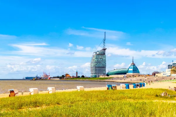 Ein kleiner Sandstrand nahe der Stadt mit einigen Strandkörben, Gras und dem Meer, im Hintergrund ist die Kulisse der Stadt.