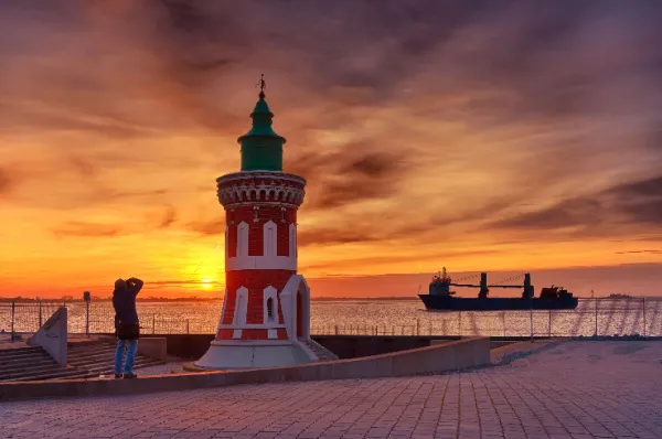 Ein fulminanter Sonnenuntergang über Bremerhaven und ein Mann der einen kleinen, rot-weißen Turm fotografiert.
